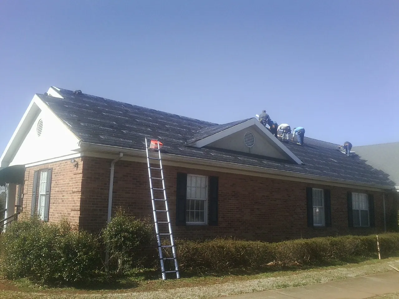 Crew tearing shingles off a brick ranch roof with a ladder set — Emergency Roof Repair work by our crew in Hastings