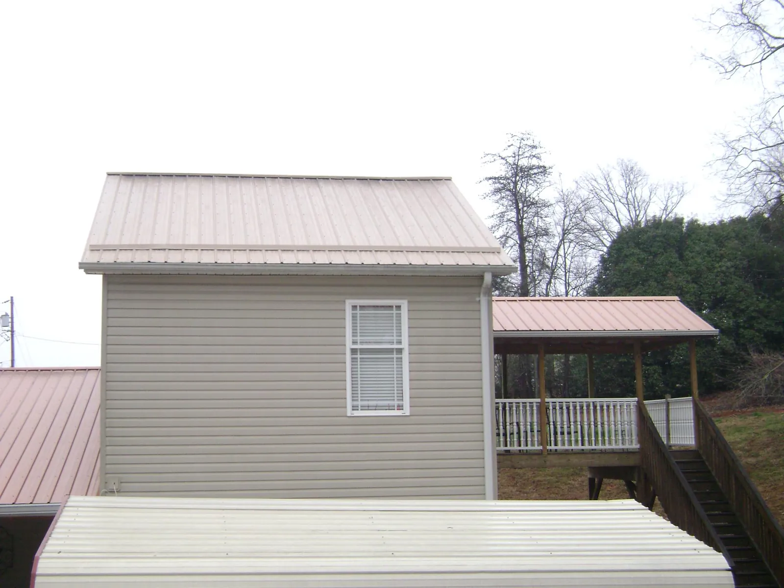 Tan metal roofs on a two story addition and attached porch, from a Roof Replacement job in Hastings